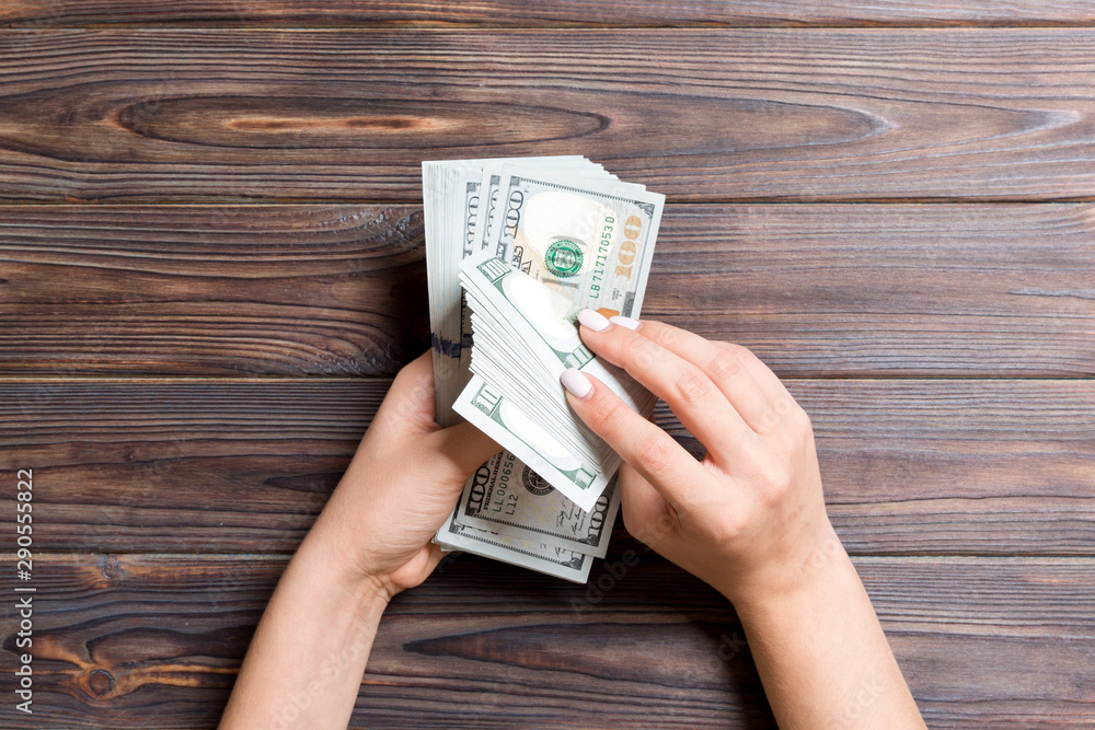 Top view of a businesswoman's hands counting one hundred dollar banknotes on wooden background. Success and wealth concept Top view of a businesswoman's hands counting one hundred dollar banknotes on wooden background. Success and wealth concept