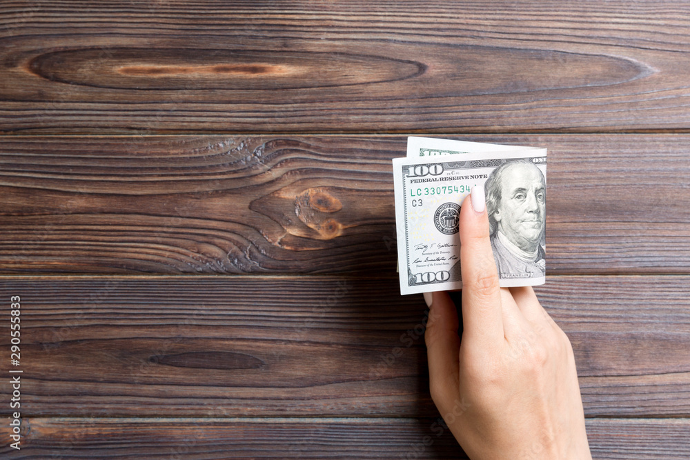 A pack of one hundred dollar bills in female hand on wooden background. Salary concept with copy space A pack of one hundred dollar bills in female hand on wooden background. Salary concept with copy space