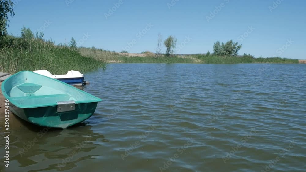 Summer day. The boat is swinging on the small waves of a small pond. Clear blue sky, reeds rustle, light wind, blue water, sunny day.