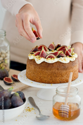 Cream covered sponge cake with figs and pistachios and with one hand placing a fig