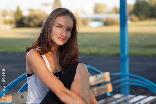 Pretty girl sits on bench in summer park