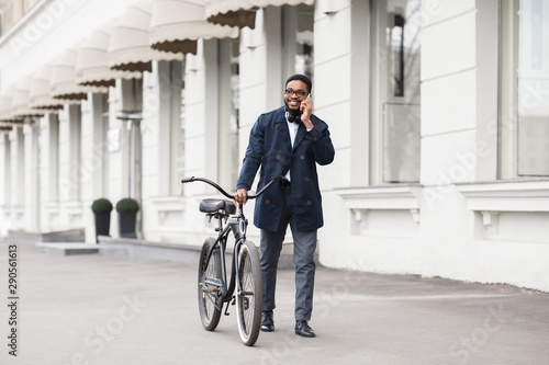 Afro businessman walking with bike and talking on phone