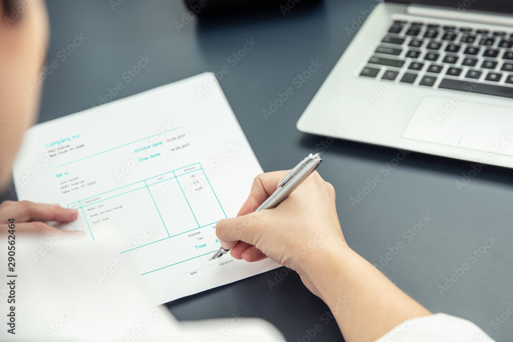 Businesswoman signs an invoice with a pen in her office Businesswoman signs an invoice with a pen in her office