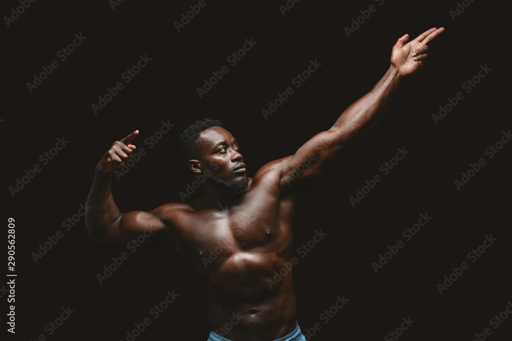 Artistic black bodybuilder posing over black background