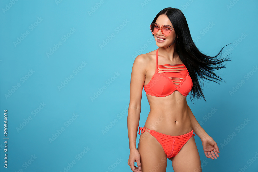 Fototapeta premium Beautiful young woman in stylish bikini with sunglasses on light blue background