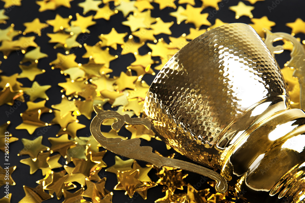 Gold trophy cup and confetti on black background, closeup. Space for text