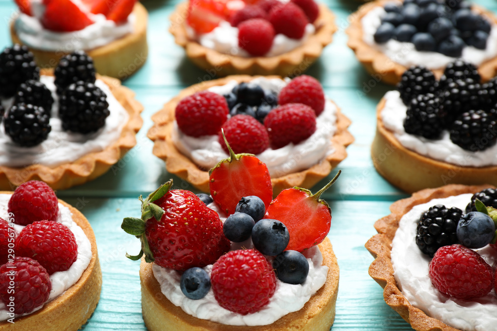 Many different berry tarts on blue wooden table. Delicious pastries Many different berry tarts on blue wooden table. Delicious pastries