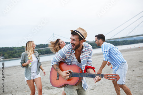 Group of friends hangout at the city beach.One guy plays guitar and singing while his friends dancing around him. © BalanceFormCreative