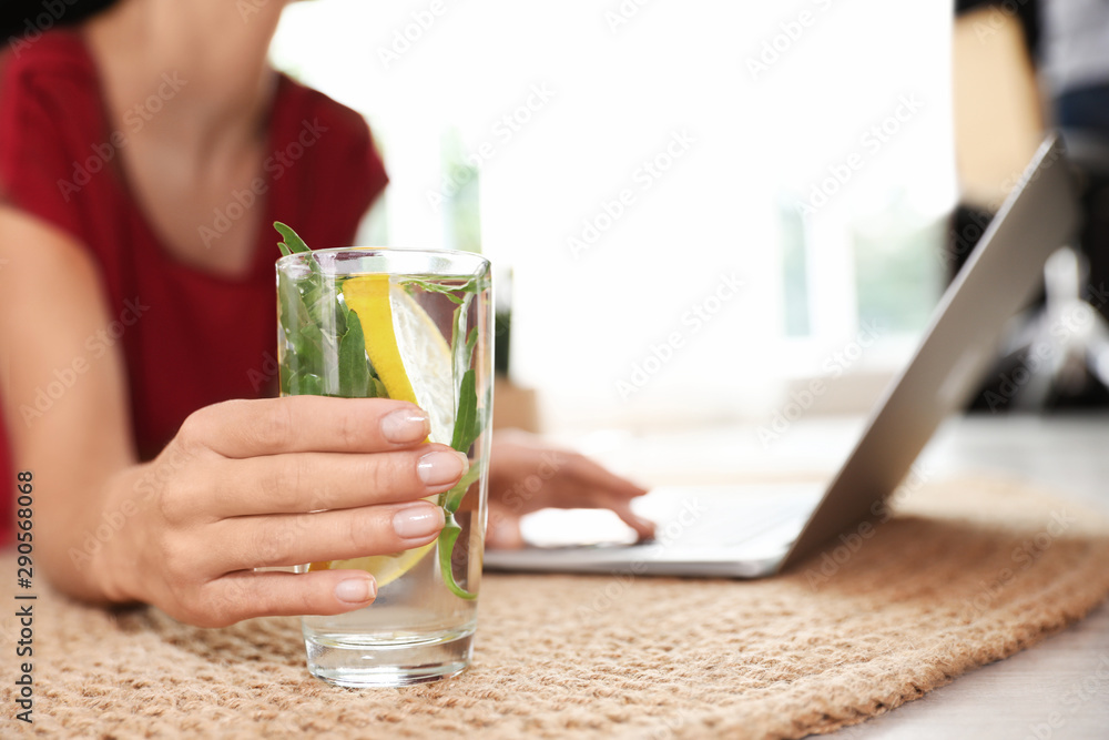 Young woman with glass of lemonade working on laptop at home, closeup. Refreshing drink Young woman with glass of lemonade working on laptop at home, closeup. Refreshing drink
