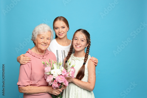 Happy sisters with their grandmother holding flowers on light blue background