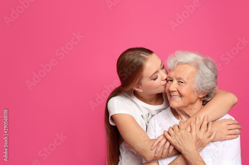 Young woman kissing her grandmother on pink background. Space for text photo