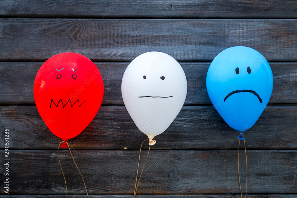 Naklejka Negative emotions concept. Balloons with drawn faces on dark wooden background top view