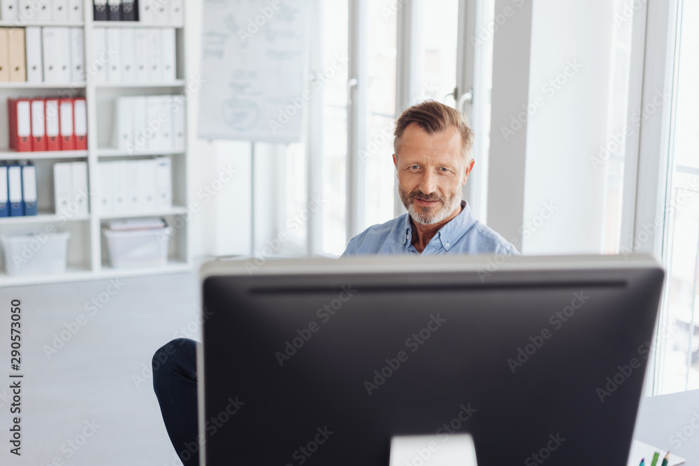 Businessman working behind a large desktop monitor Businessman working behind a large desktop monitor