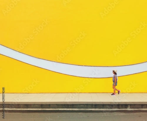 Woman walking across a walkway with abstract mural wall next to her.