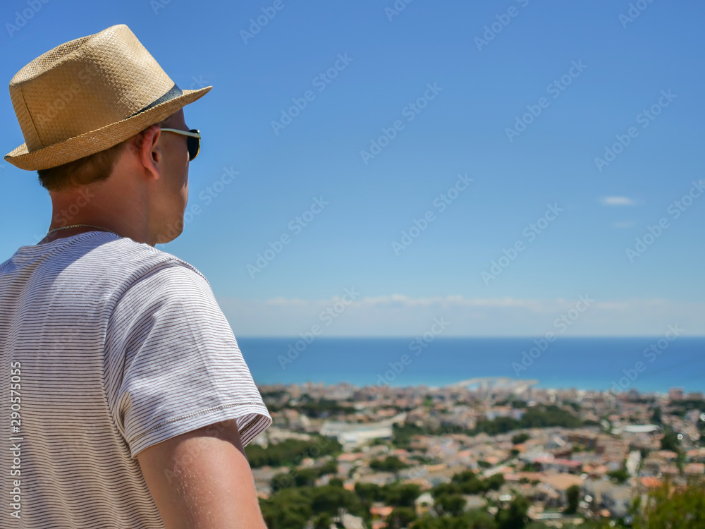 A man in a hat looks in front of him at a beautiful view of a settlement by the sea, close-up