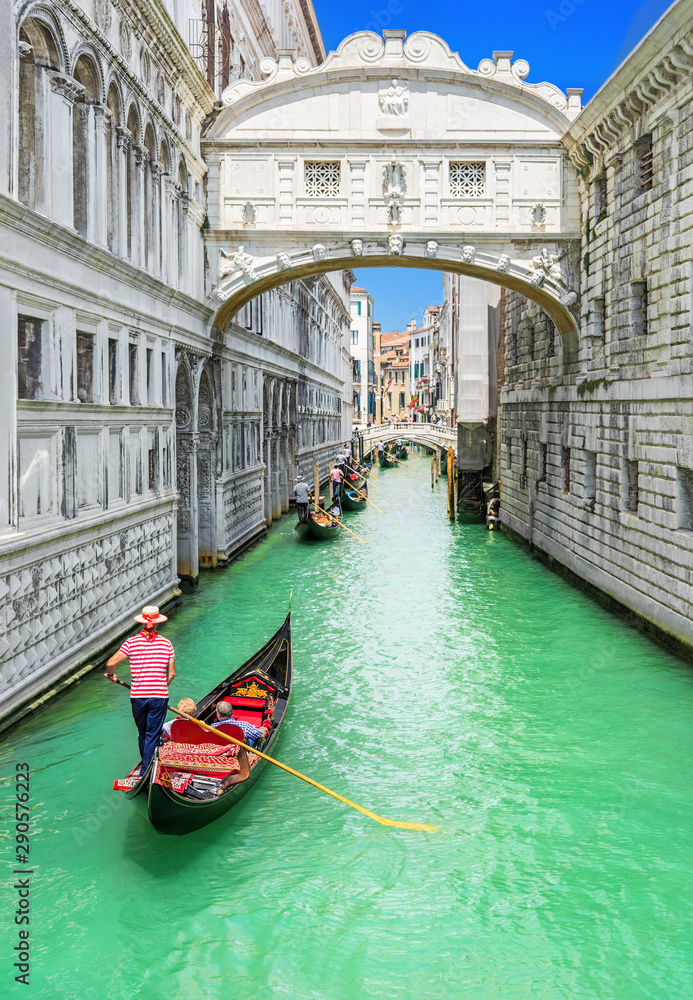 Bridge of Sighs (Ponte dei Sospiri) and row of gondolas with gondoliers and Rio de Palazzo o de Canonica Canal from Riva degli Schiavoni in Venice, Italy. Ponte de la Canonica is visible in background