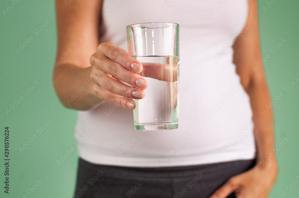 A pregnant girl holds a glass of water in her hand. Maintaining the health of mother and baby. A pregnant girl holds a glass of water in her hand. Maintaining the health of mother and baby.