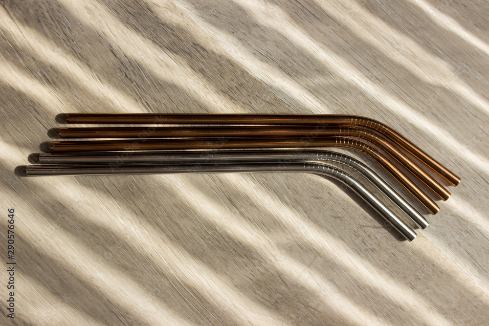 Metal straws in sun on wooden background. Zero waste. Flat lay Metal straws in sun on wooden background. Zero waste. Flat lay