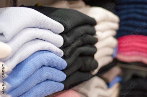 Warm clothing neatly folded on a store shelf. Sweatshirts, sweaters, jumpers, cardigans, hoodies, bobmers with piles on the shelf. Clothes storage. Size range.