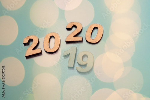 The inscription 2020 is bright and 2019 is dim, a sign of the outgoing year. New Year and Christmas, from behind blurred dots of light on a blue background and red balls on Christmas tree. 