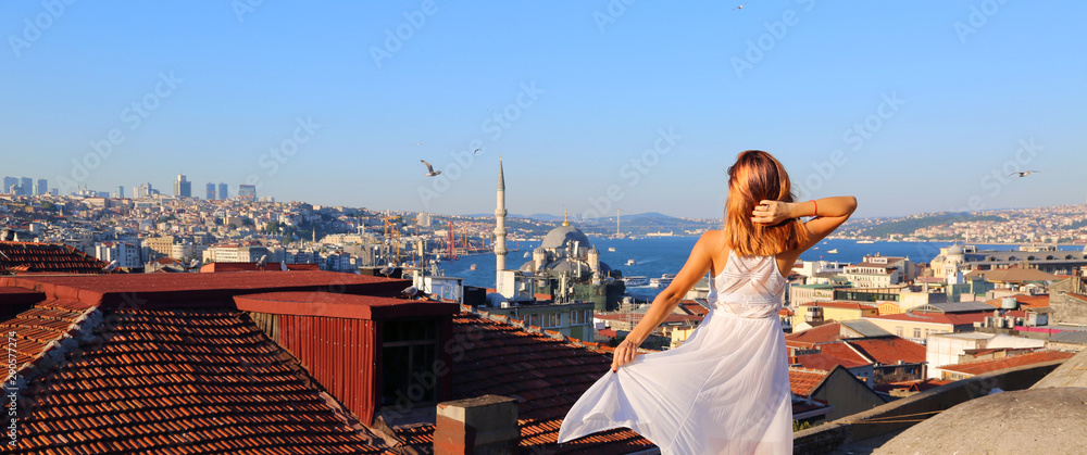 Fototapeta premium Happy young woman standing on the rooftop in Istanbul Turkey. Back view of the girl in white long dress at the famous tourist attraction of Istanbul. Travel, tourism, excursions.