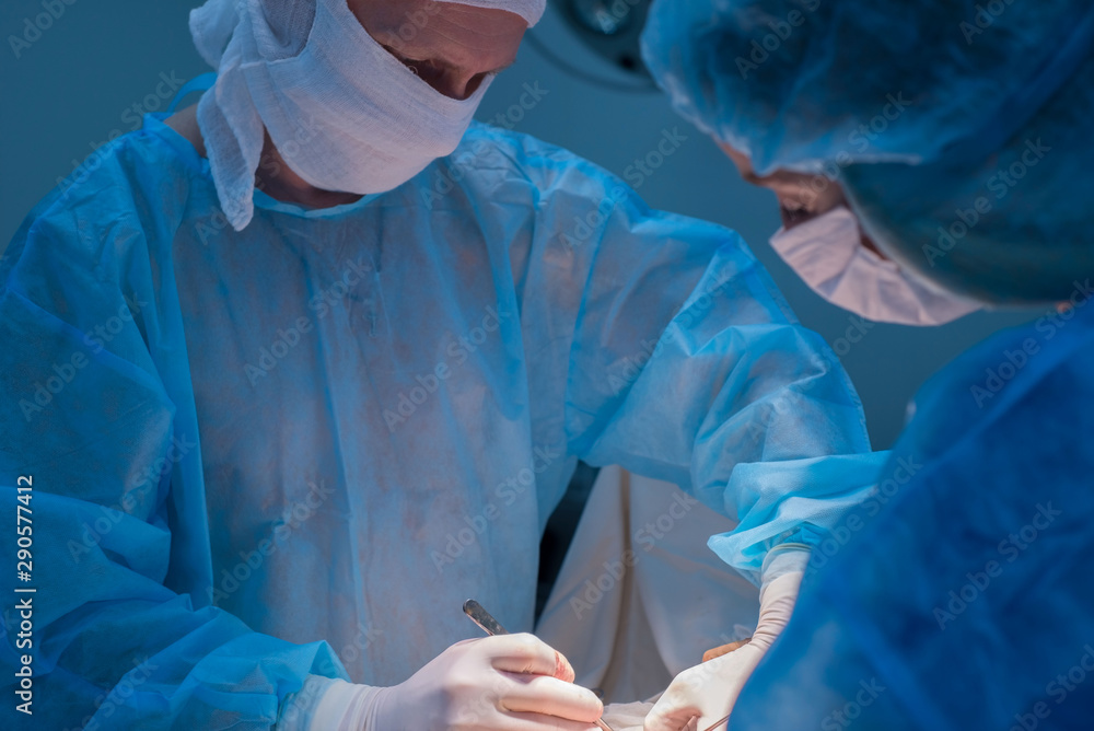 Children's surgeons perform urological surgery. A man and a woman in a mask, and a blue sterile gown, in the operating room. Children's surgeons perform urological surgery. A man and a woman in a mask, and a blue sterile gown, in the operating room.