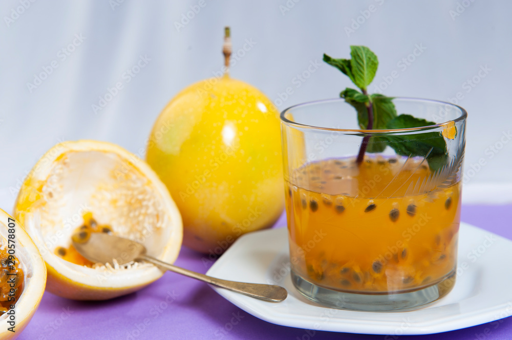 Passion fruit juice, in the foreground, focused. Passion fruit, in the background, blurred. Natural calming.Close view.Cassis color background. Passion fruit juice, in the foreground, focused. Passion fruit, in the background, blurred. Natural calming.Close view.Cassis color background.