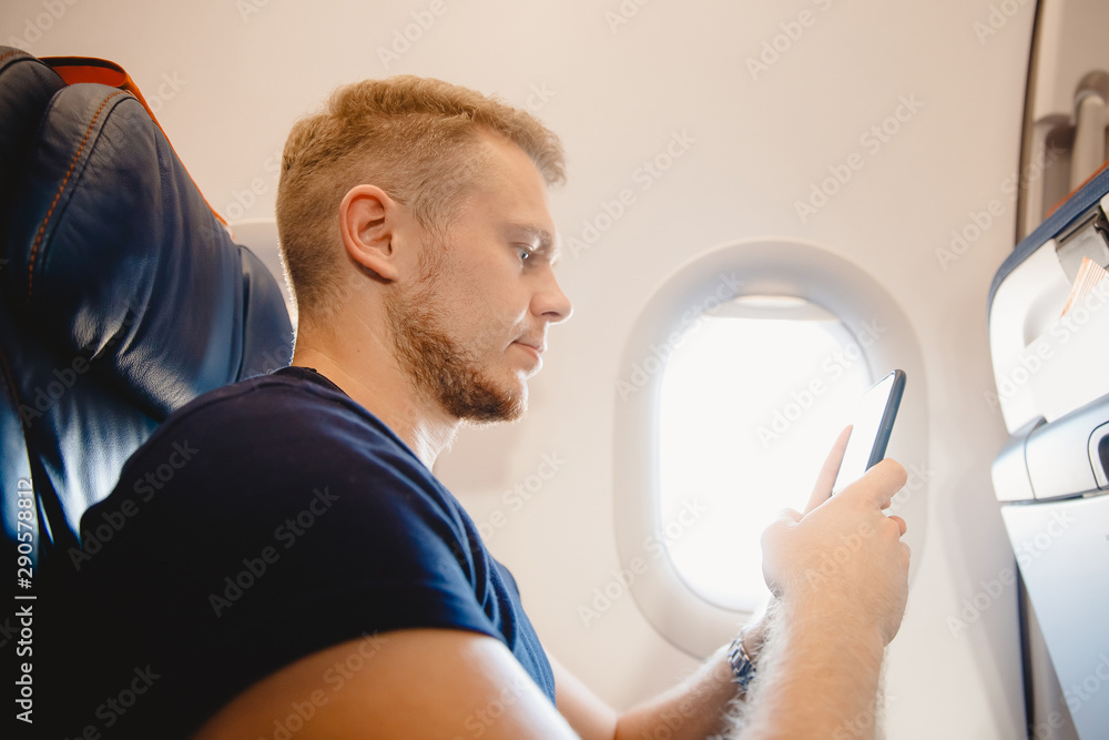 Obraz premium Man uses smart mobile phone in cabin airplane, concept Internet in air stratosphere