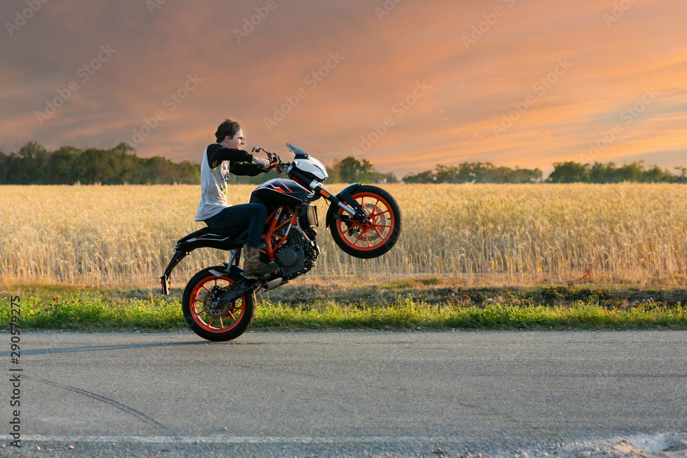 Teenage boy on a dirtbike motorcycle doing a wheelie at sunset - obrazy, fototapety, plakaty 