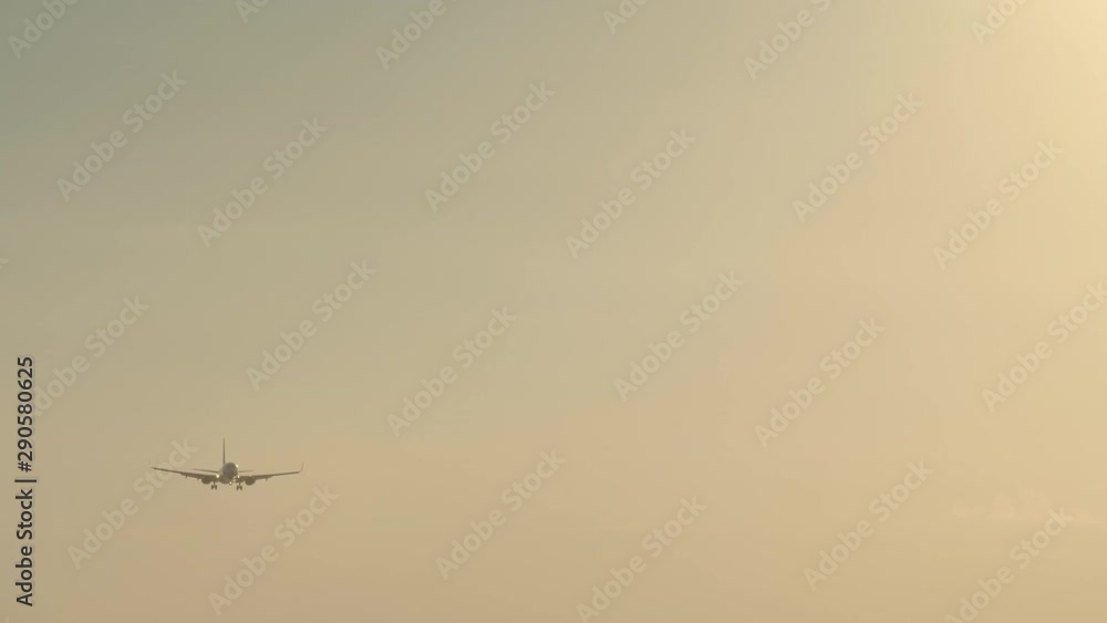 Silhouette of small civil jet plane is landing in airport in windy weather during sunset