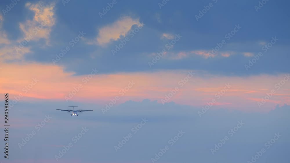 Silhouette of small turbo jet airplane is landing with head light in yellow blue sunset with clouds Silhouette of small turbo jet airplane is landing with head light in yellow blue sunset with clouds
