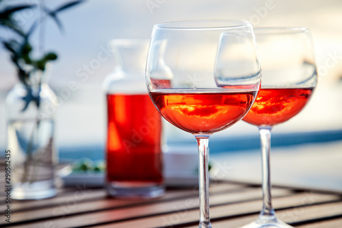 two glasses of rose wine with olives against blue water on a pier..