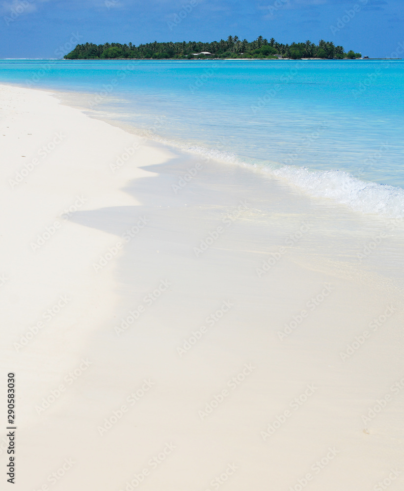 Fototapeta premium Beautiful white sand Maldivian beach and absolutely clear blue waters of Indian Ocean with a tropical paradise island on the background