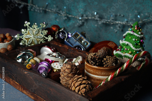 Wooden box with New Year's toys, pine, spruce, cedar cones, knitted Christmas tree, glass machine, openwork snowflake-Christmas tree toy, nuts in a ceramic cup and a garland.