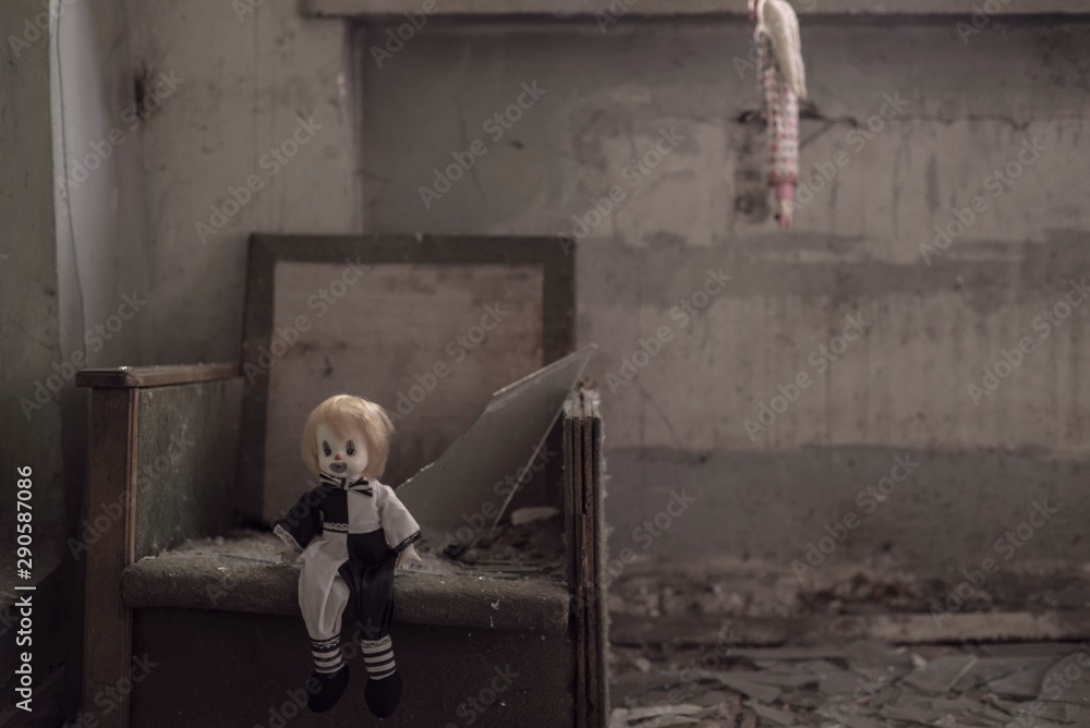 Fototapeta premium Halloween background A terrible harlequin doll sitting in a chair, a second doll hangs on a second background. Theme for horror. Mystical art photography. The concept of loneliness, abandonment