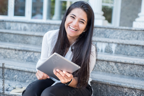 Portrait of a beautiful young Indian girl, business woman, smiling, sitting on the steps, looking into tablet