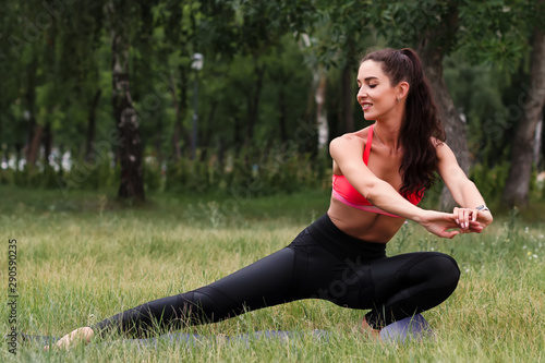 Young attractive smiling toned brunette woman stretching outside in a park. Healthy lifestyle concept
