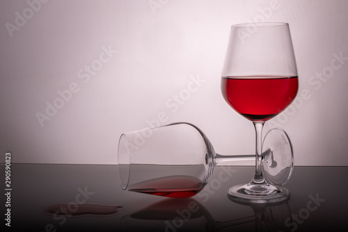 two red wine glasses on a white background, one glass half full the second lies, spilled wine