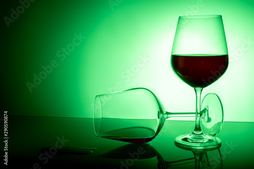 two red wine glasses on a white background, one glass half full the second lies, spilled wine