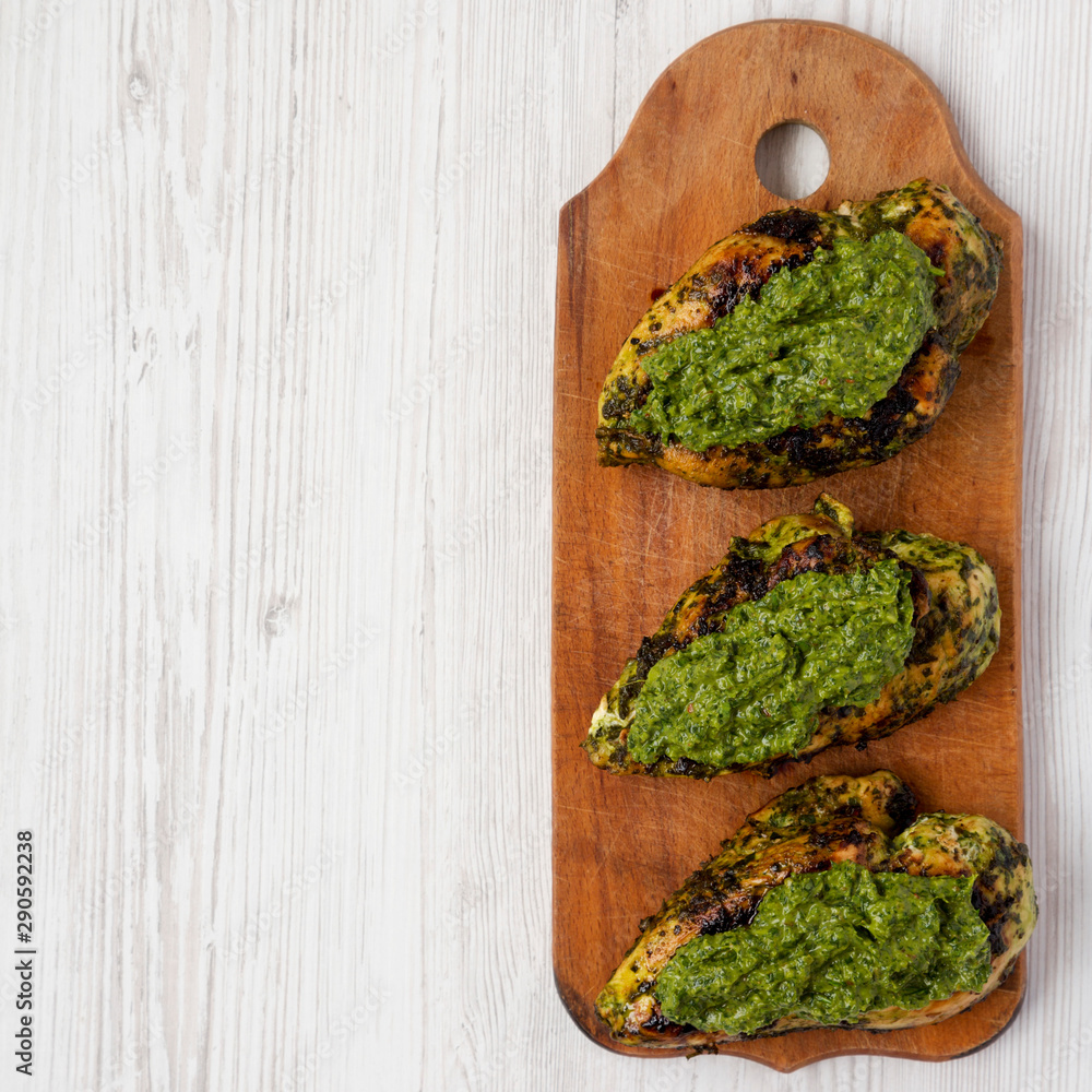 Grilled chimichurri chicken breast on a rustic wooden board on a white wooden table, top view. Flat lay, overhead, from above. Space for text. Grilled chimichurri chicken breast on a rustic wooden board on a white wooden table, top view. Flat lay, overhead, from above. Space for text.