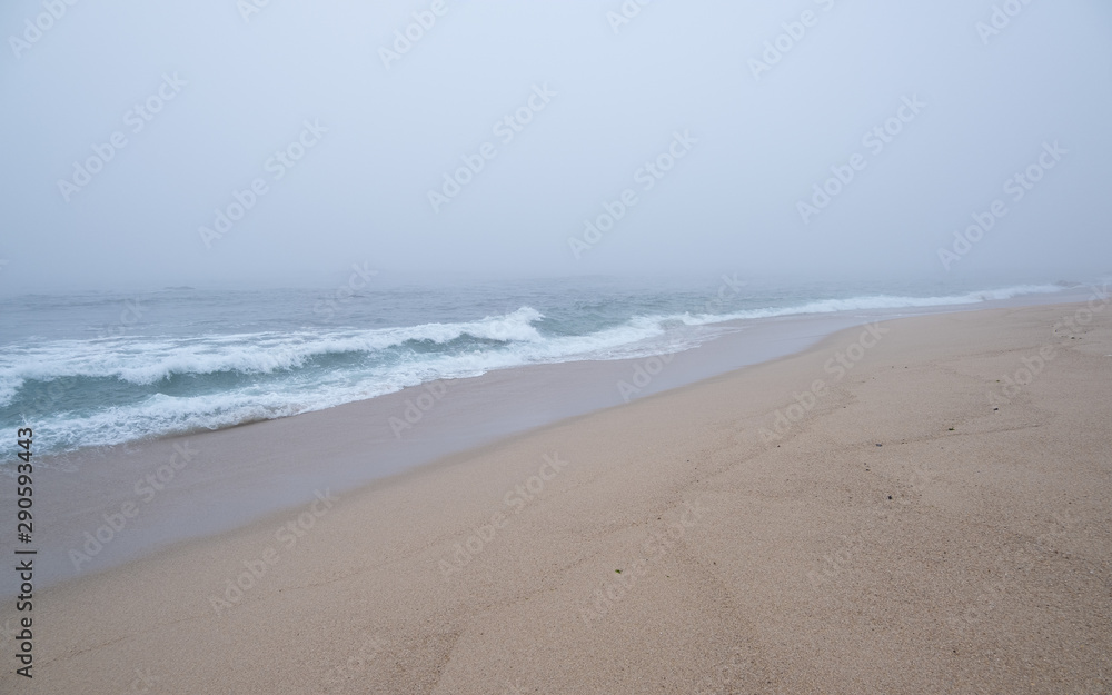 Thick, dense fog over the ocean as waves break on the empty, sandy beach.