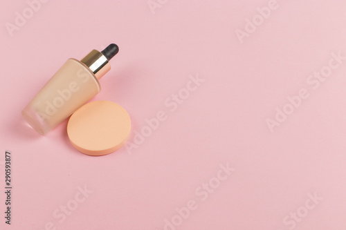 Sponges, a beautiful blender for applying foundation or powder and a bottle of concealer. Flat lay on a pink background, copy space.