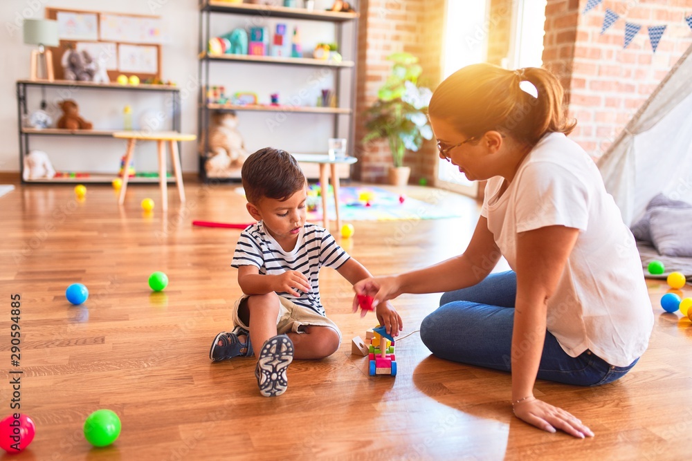 Fototapeta premium Beautiful teacher and toddler boy playing with train at kindergarten