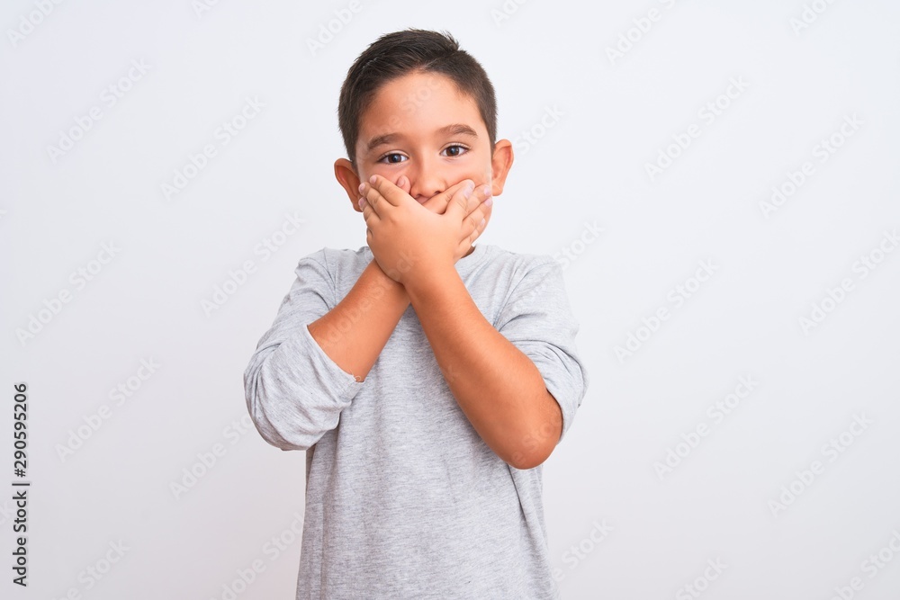Beautiful kid boy wearing grey casual t-shirt standing over isolated white background shocked covering mouth with hands for mistake. Secret concept. Beautiful kid boy wearing grey casual t-shirt standing over isolated white background shocked covering mouth with hands for mistake. Secret concept.