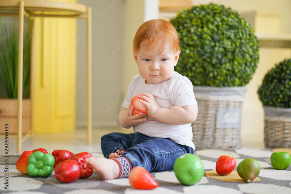 Fototapeta premium chubby fatty baby child with plus size body and red hair plays with vegetables and like his diet on room background