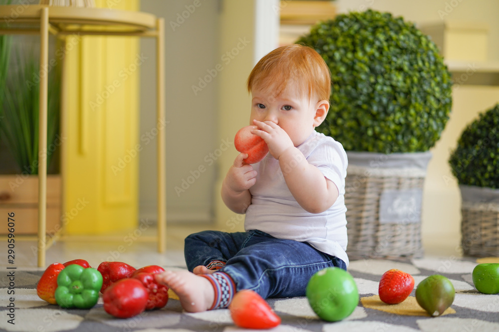 Fototapeta premium chubby child with red hair plays with vegetables