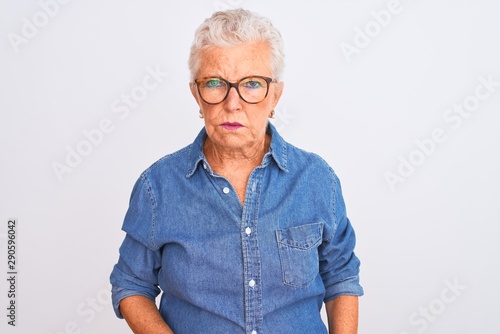 Senior grey-haired woman wearing denim shirt and glasses over isolated white background skeptic and nervous, frowning upset because of problem. Negative person.