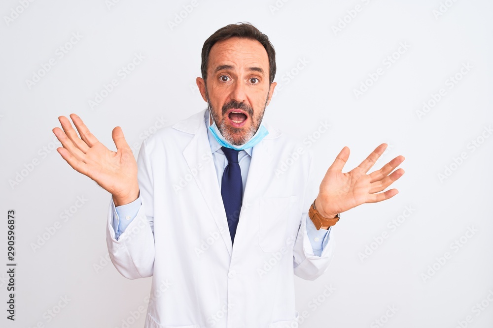 Middle age scientist man wearing coat and medical mask over isolated white background clueless and confused expression with arms and hands raised. Doubt concept. Middle age scientist man wearing coat and medical mask over isolated white background clueless and confused expression with arms and hands raised. Doubt concept.
