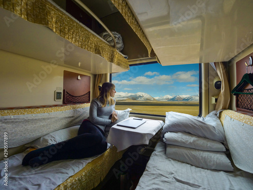 Young woman lies on the bed and looks through the window of the sleeper train.