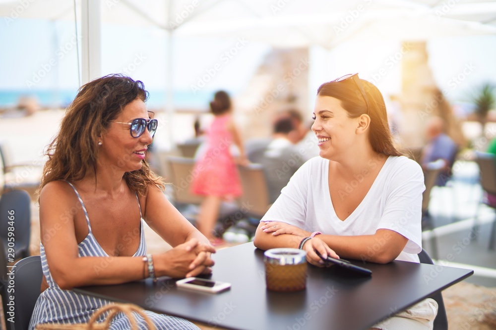 Beautiful mother and daugther sitting at terrace of a restaurant speaking and smiling Beautiful mother and daugther sitting at terrace of a restaurant speaking and smiling